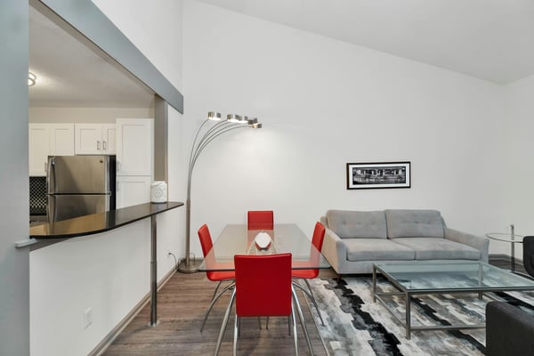 Open-plan living room and kitchen with beige sofas, glass coffee table, white cabinetry, and wood-look flooring